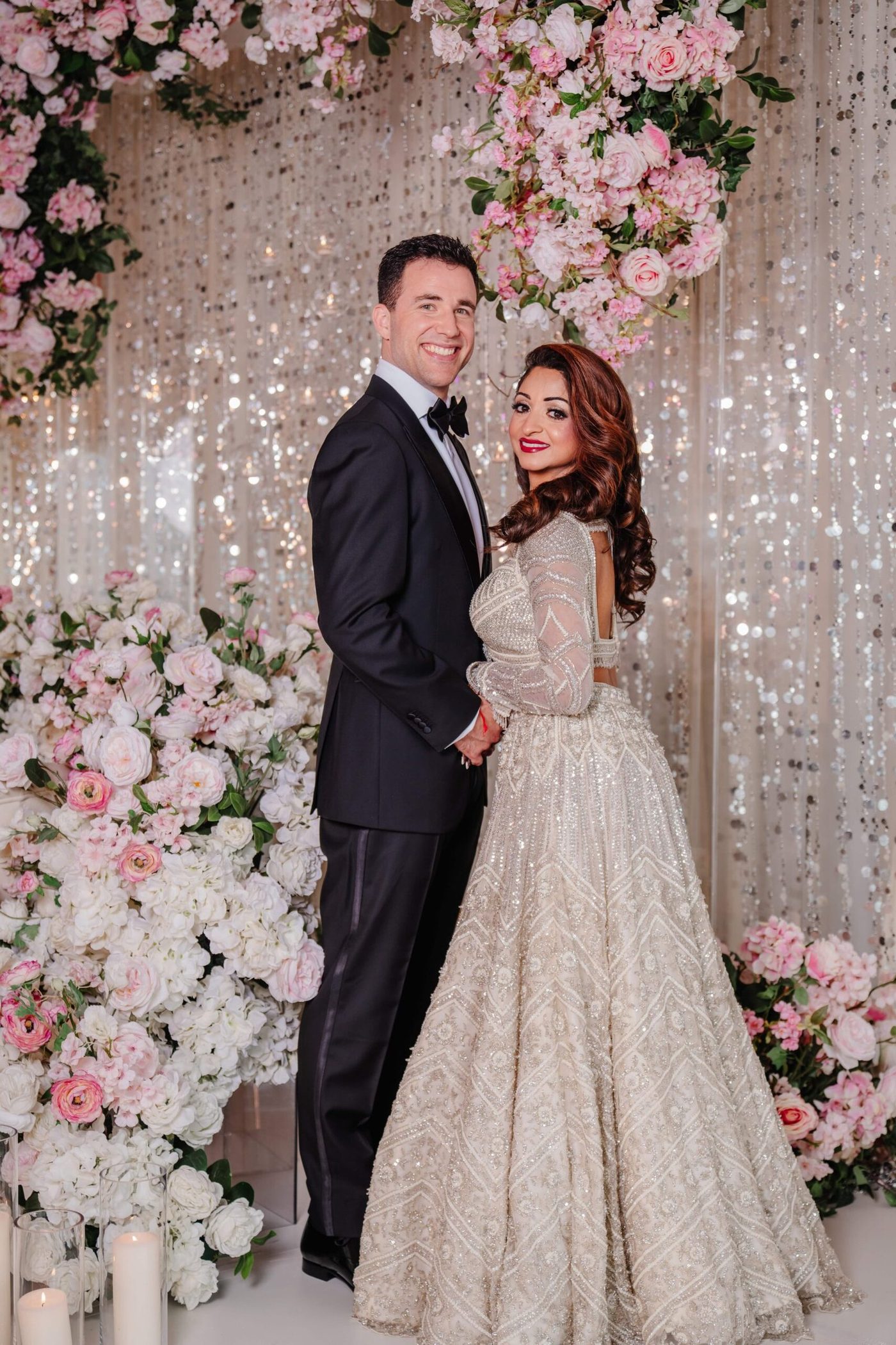 Modern couple in tuxedo and gown by a floral wall